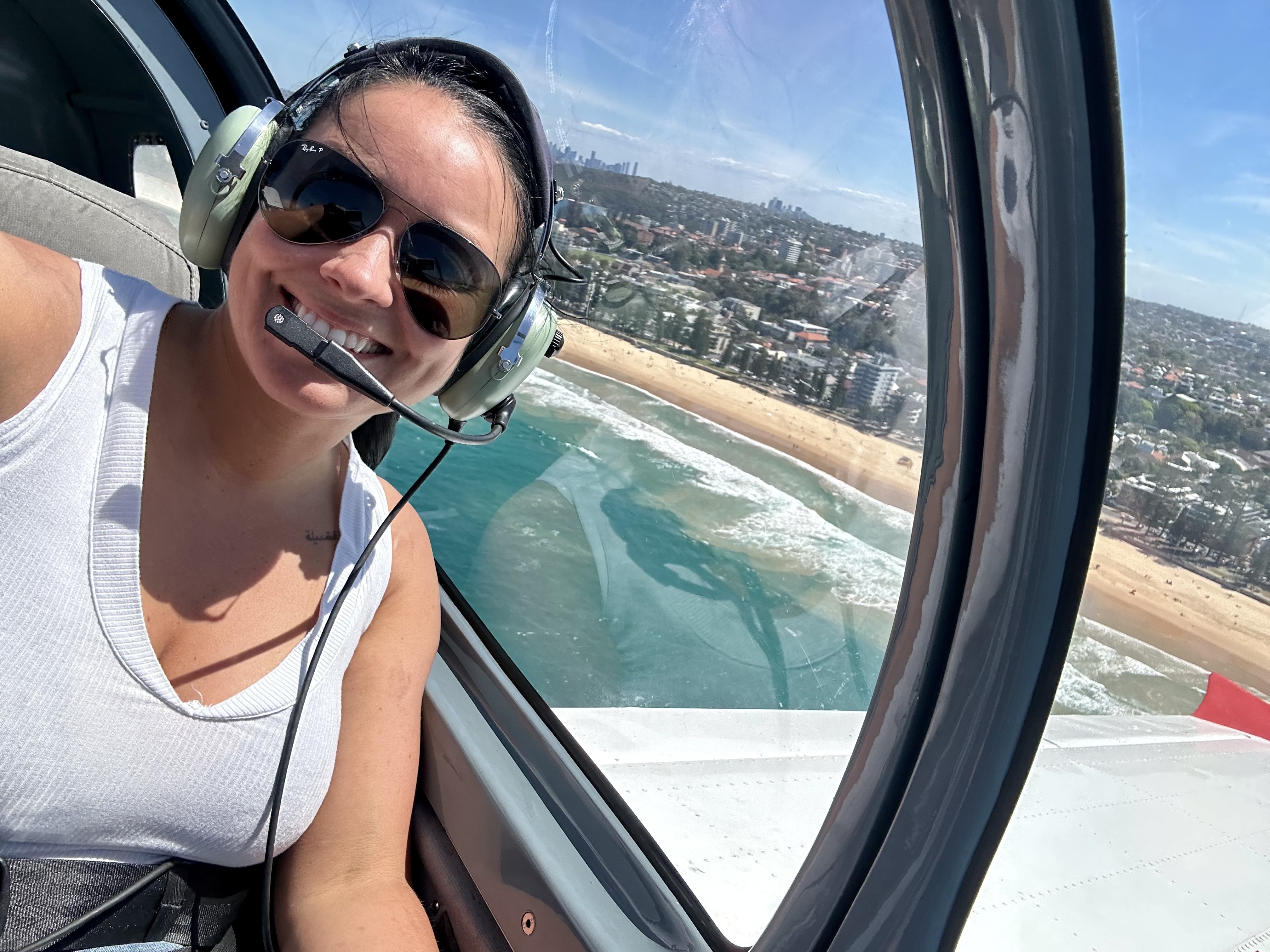 Rebecca in a headset in the cockpit of a light aircraft above the Sydney coastline