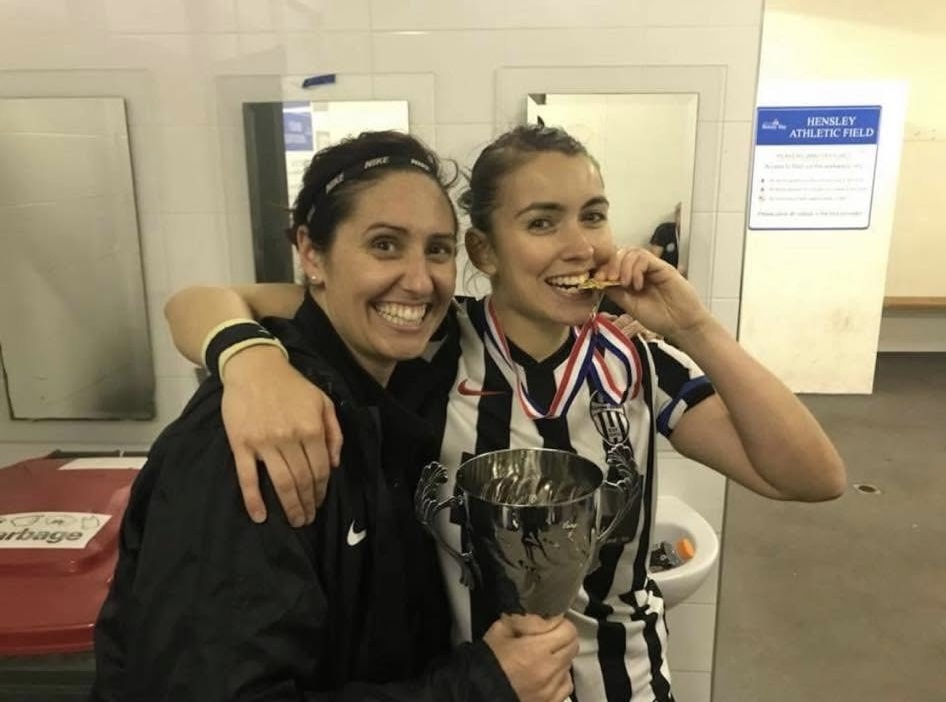 Rebecca biting her medal and holding a trophy in the changing rooms after winning