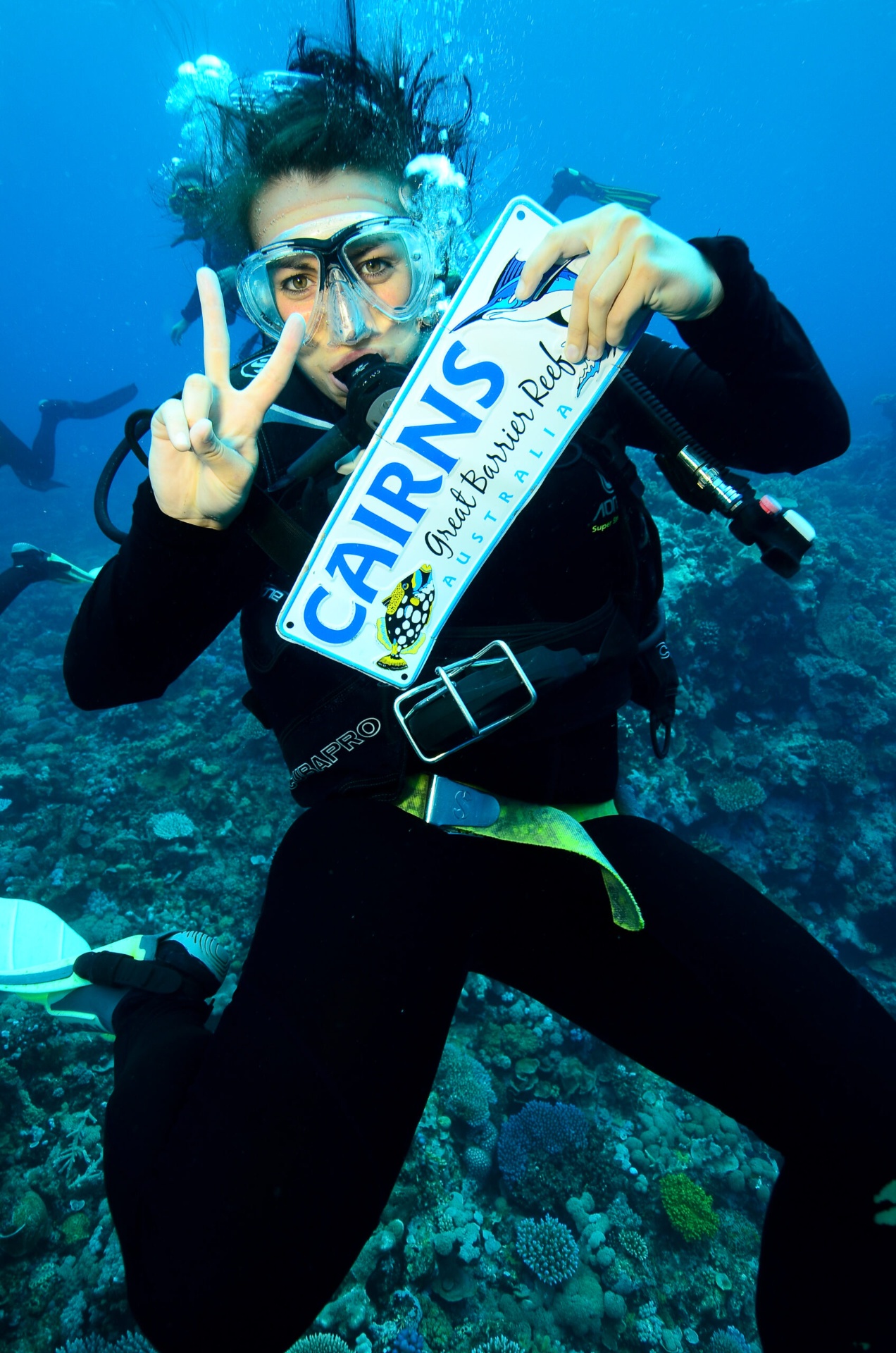 Rebecca scuba diving over a coral reef holding a Great Barrier Reef souvenir plate