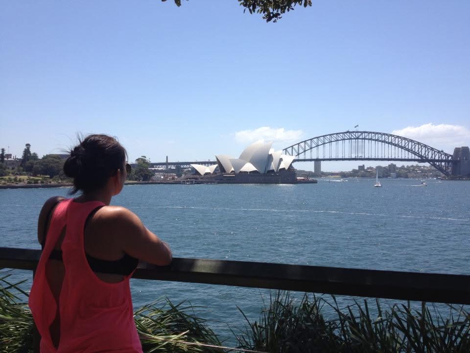 Rebecca leaning on a railing looking out at the Sydney Opera House and Harbour Bridge
