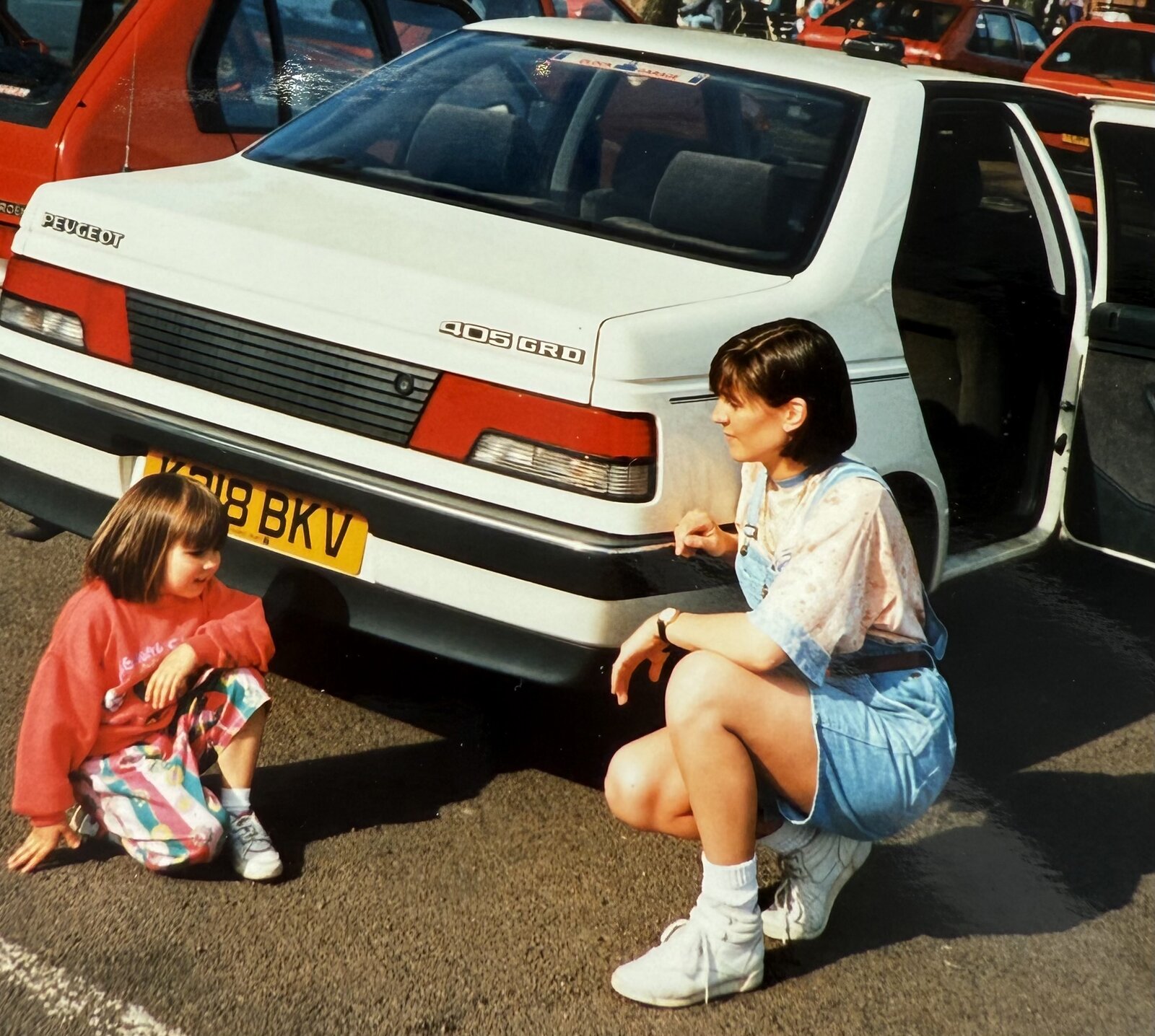Young Rebecca sitting with her mum beside a white car