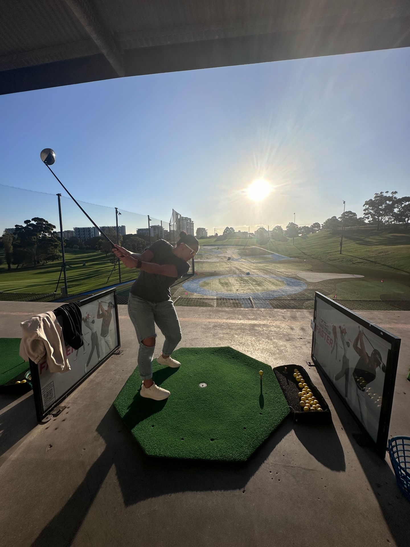 Rebecca mid-swing at a floodlit golf driving range at sunset