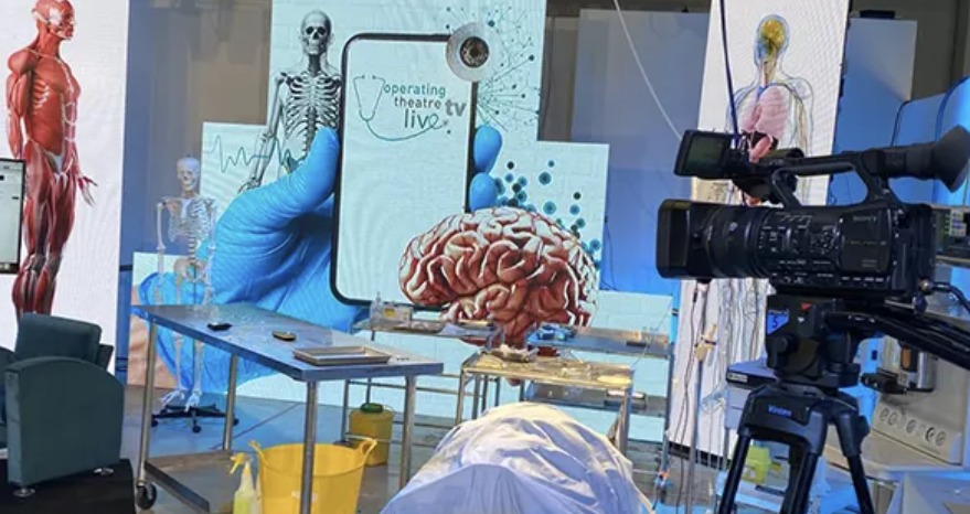 A television studio set built for live medical education, with a broadcast camera in the foreground and anatomical screens behind