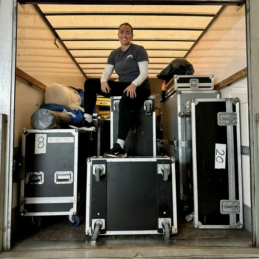 Rebecca sitting on stacked road cases inside a production truck, smiling at the camera